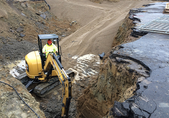 An employee operates an excavator in a pit of dirt and sand.