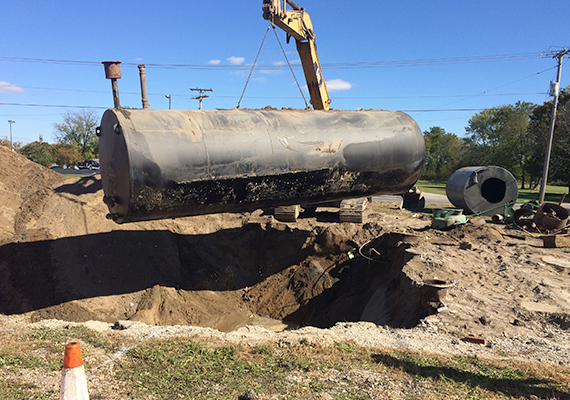 A black tank being hoisted out of the dirt by a crane.